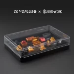 Clear acrylic-topped ZOMOPLUS X BugerWork metal keycap box showcasing various artisan keycaps, offering enhanced visibility from all angles.